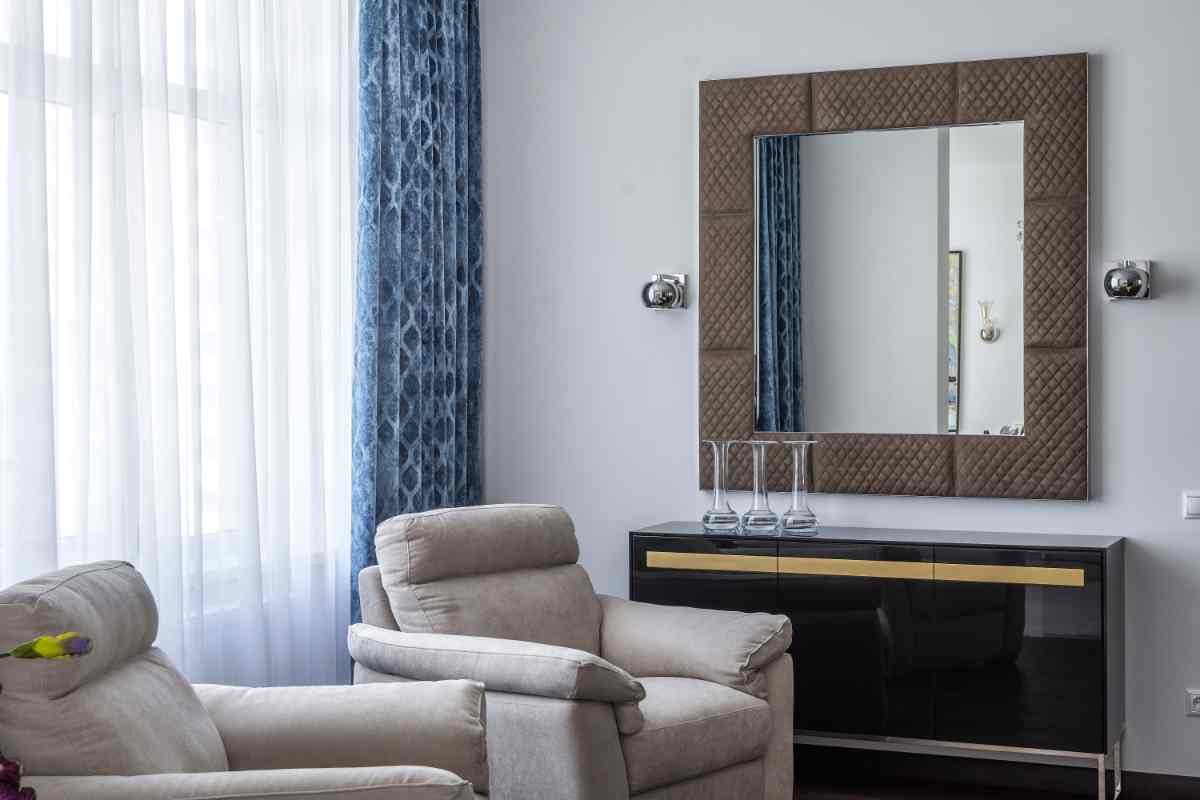 soggiorno con poltrone e grande specchio con cornice in tessuto