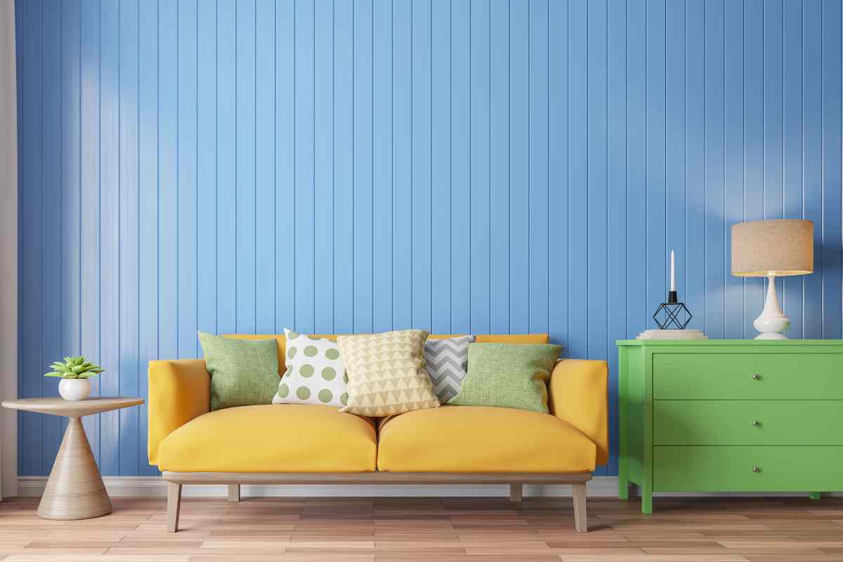 soggiorno con parete azzurra, divano giallo e cassettiera verde, esempio di come abbinare colori di mobili diversi