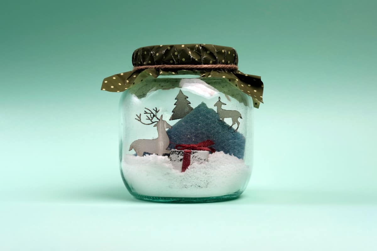 barattolo in vetro con paesaggio natalizio all'interno con renne, montagna, neve e abete 