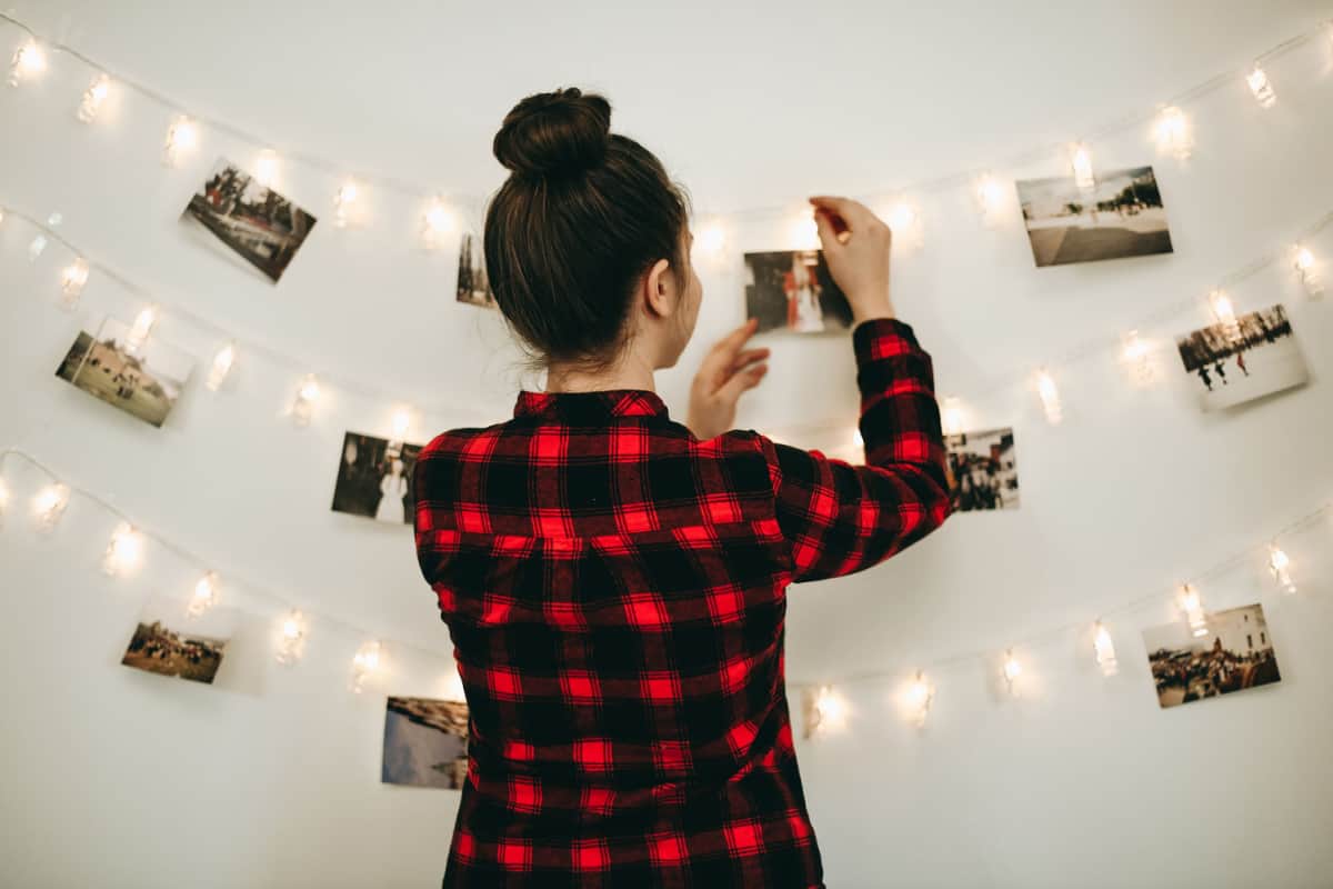 ragazza di spalle che appende delle foto polaroid al muro su file di lucine