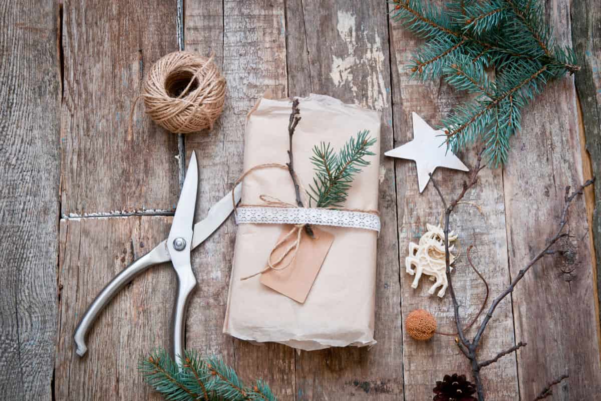 tavolo in legno con forbici, spago e regalo con carta riciclata e rametti verdi