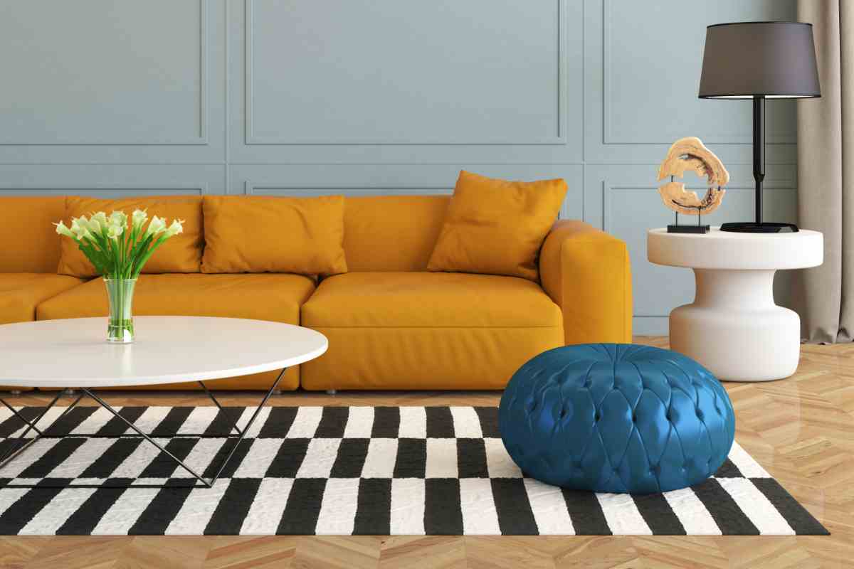 Tappeto a righe bianche e nere davanti a divano senape e pouf blu