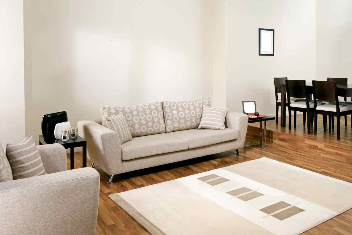soggiorno con divano e poltrona beige, cuscini con decorazioni bianche e tappeto che richiama i colori presenti