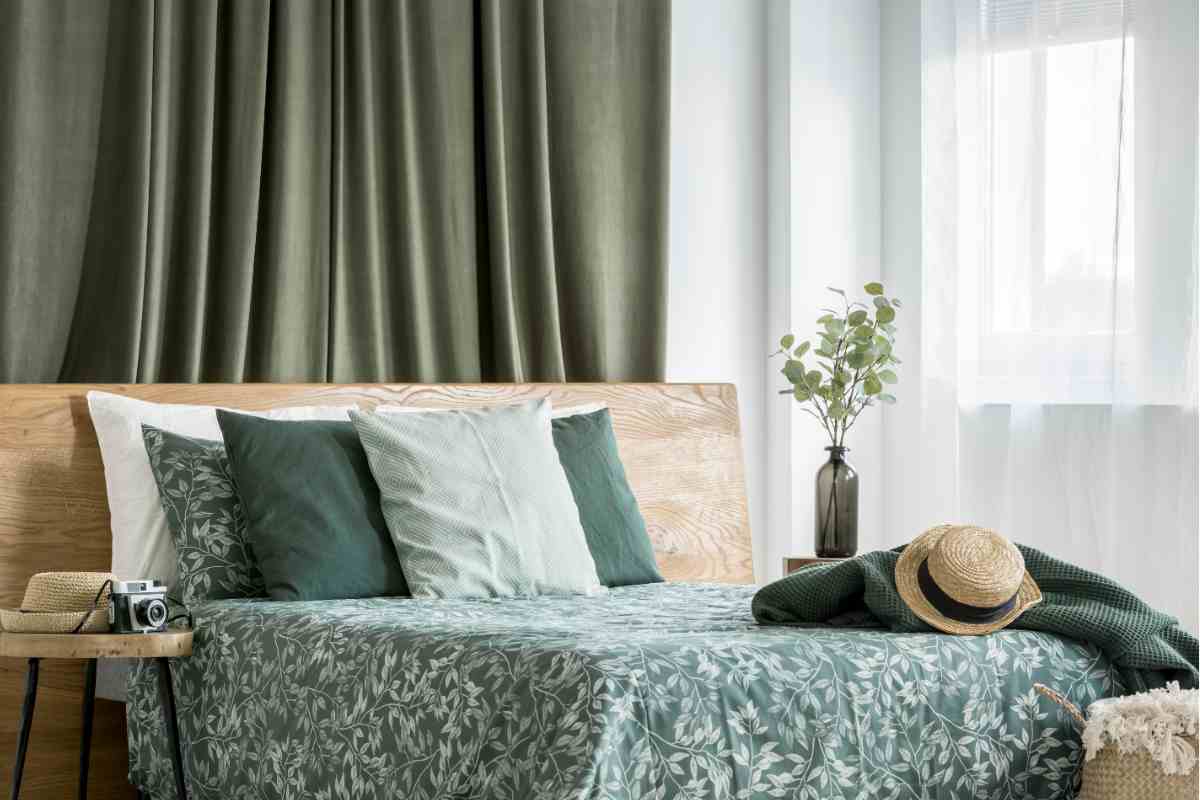 Camera da letto verde muschio con tende oscuranti e letto con biancheria floreale tono su tono