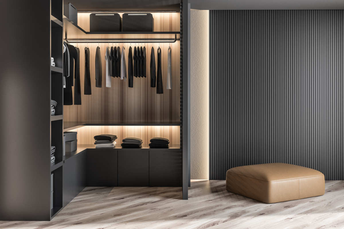 cabina armadio di colore nero, con abiti appesi, in una stanza con pareti grigio scuro, parquet chiaro e pouf beige