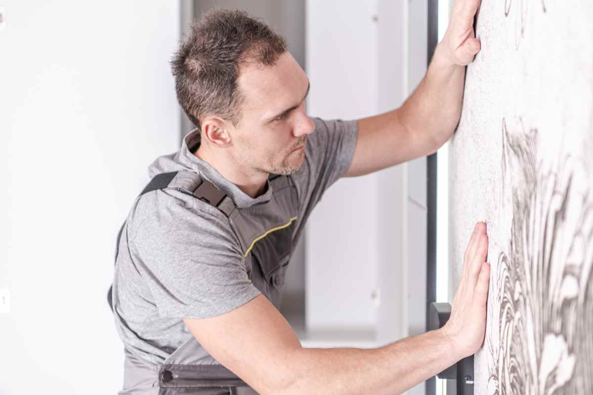 uomo con le mani sul muro pronto a decorare la vecchia carta da parati