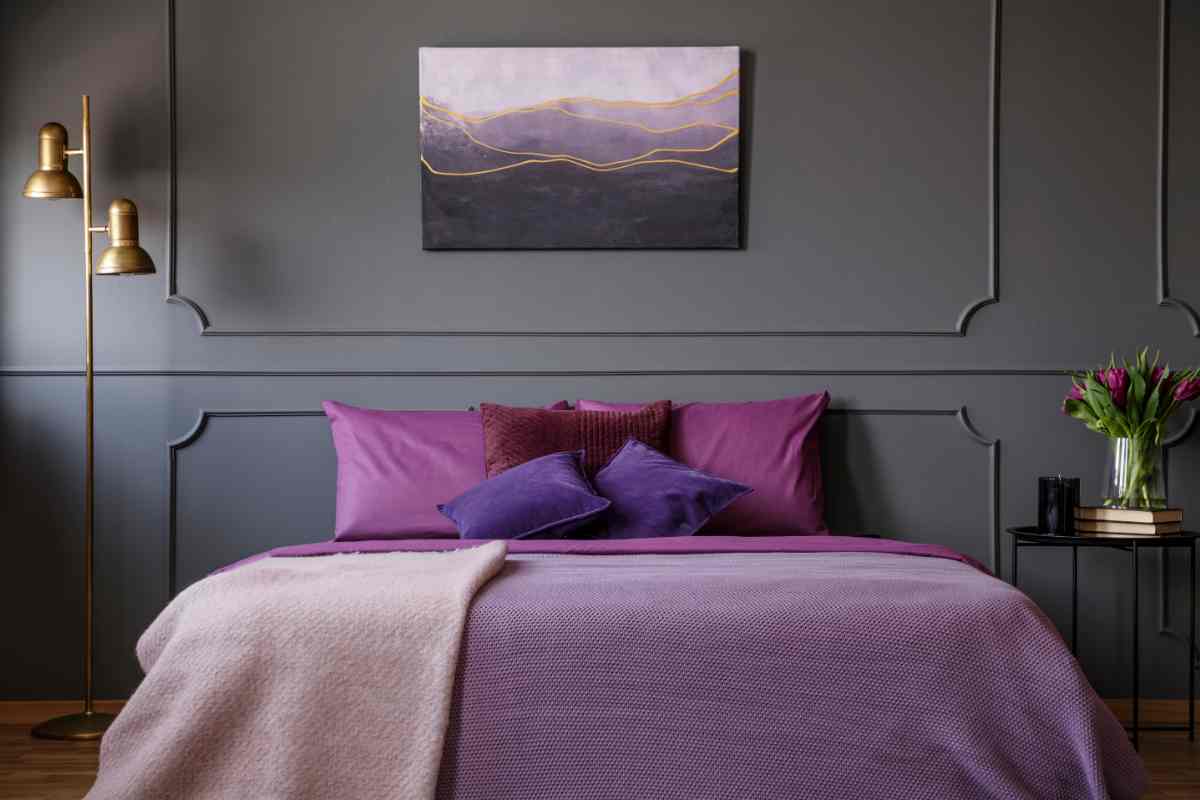 Camera da letto con boiserie grigia alla parete e biancheria viola