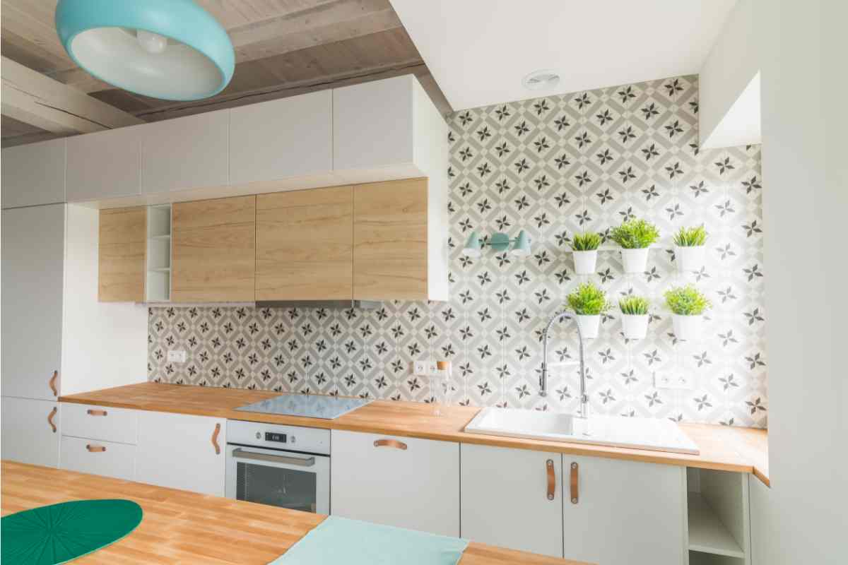 Cucina moderna con mobili bianchi e legno chiaro con vasi appesi alle pareti come simbolo di come scegliere la cucina
