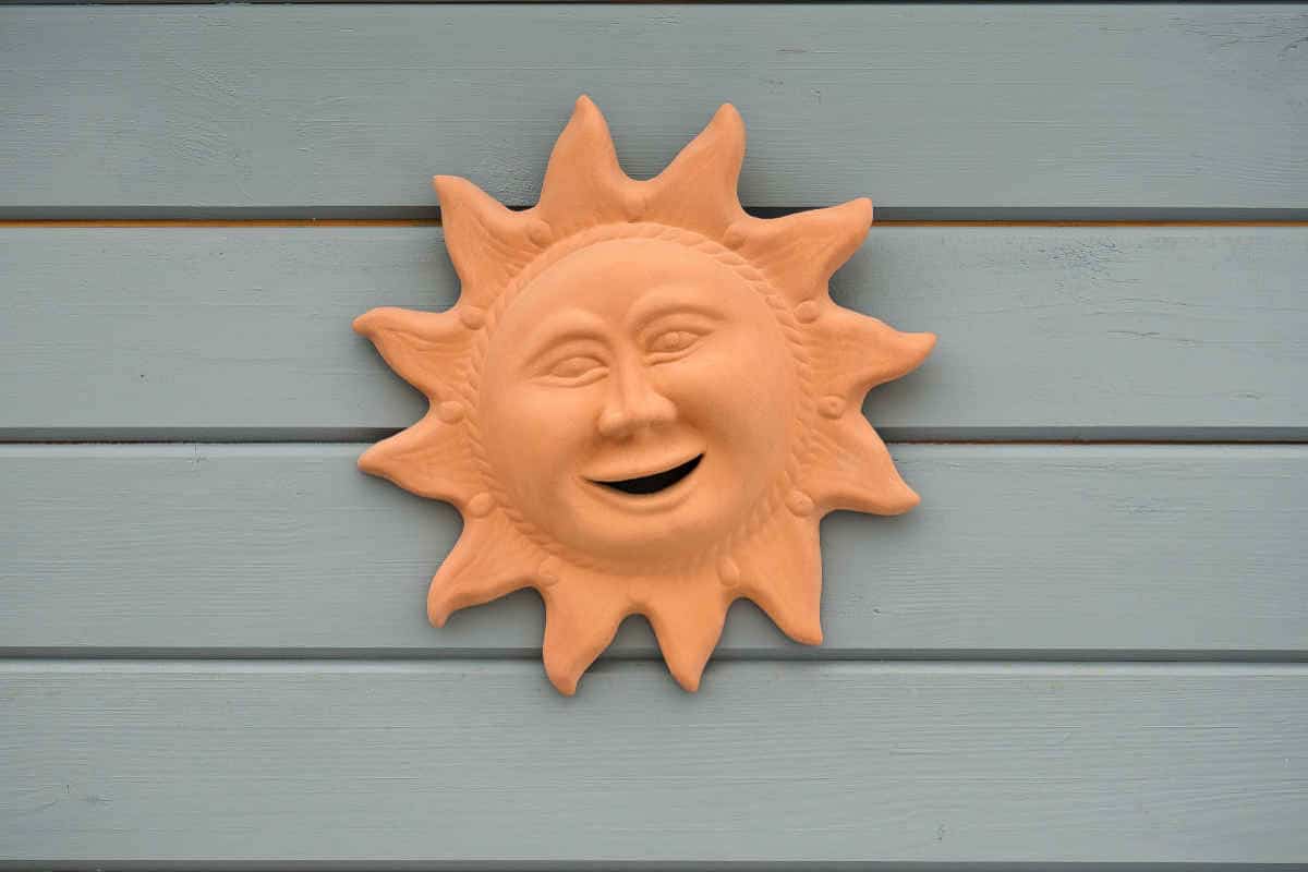 scultura in terracotta a forma di sole appesa ad una parete di colore grigio
