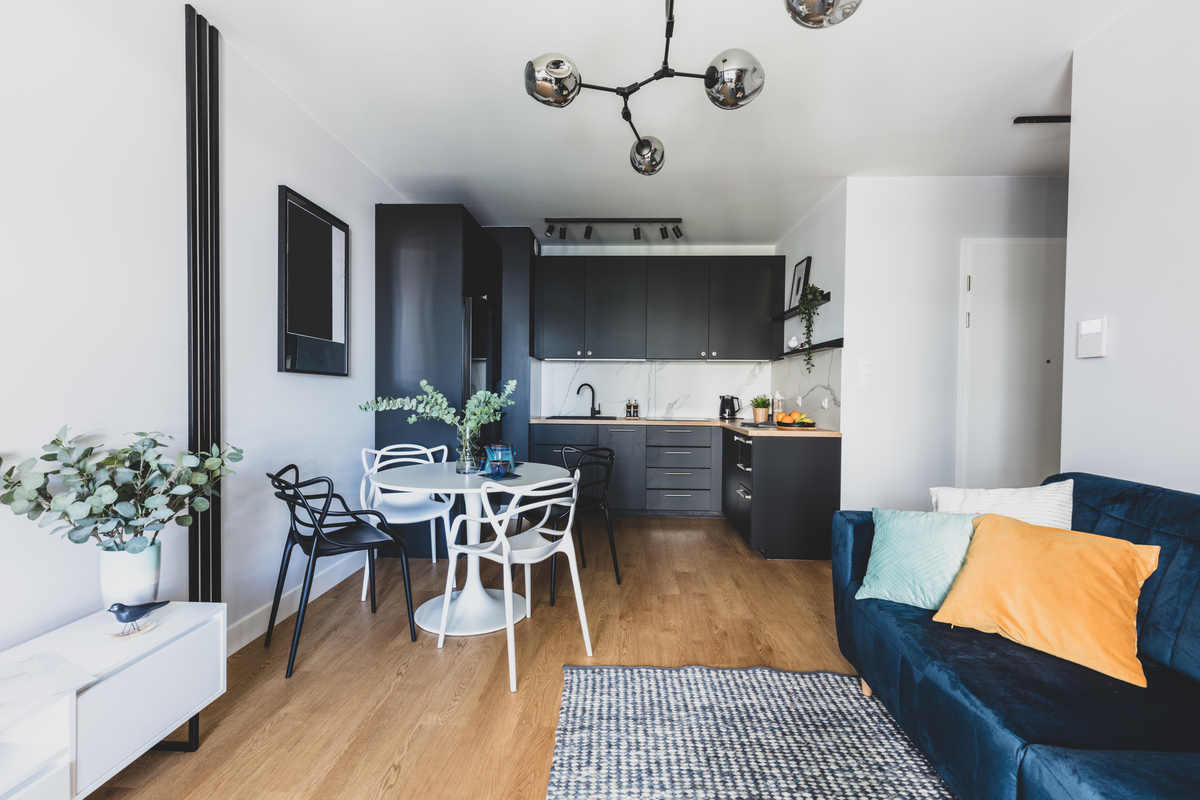 stanza con divano blu, cucina blu a muro, pavimento in parquet, con tappeto grigio, tavolo con sedie e lampadario