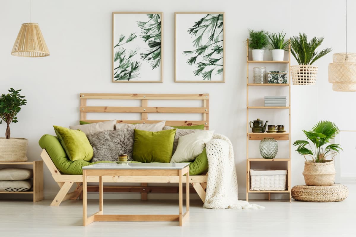 soggiorno arredato con mobili in legno chiaro, con quadri con foglie verdi, piante verdi per arredare, pareti e pavimento di colore bianco