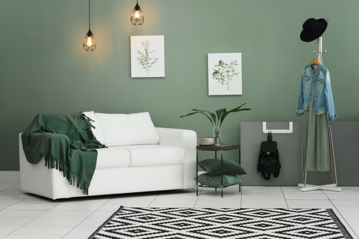 soggiorno con pareti di colore verde oliva, divano bianco, tappeto bianco e nero e complementi d'arredo vari