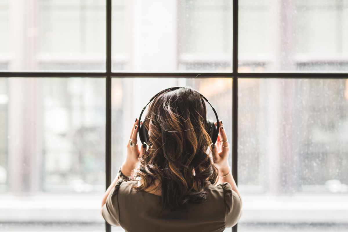 ragazza di spalle con cuffie ascolta musica di fronte alla finestra