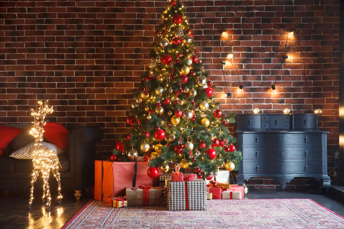 albero di natale con decorazioni di colore rosso e oro in un soggiorno con pacchi regalo e renna luminosa