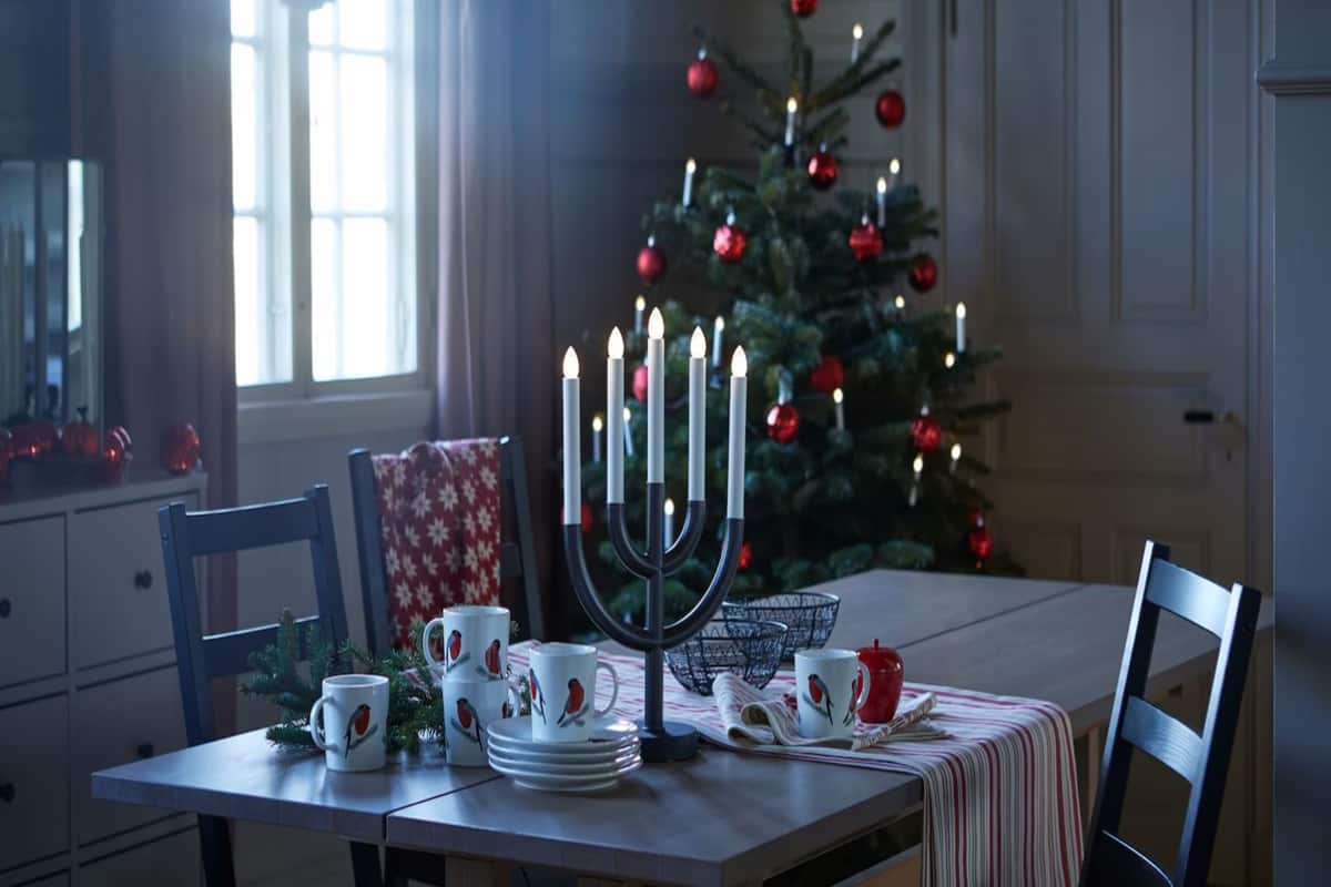 tavola decorata con arredi natalizi, tazze e runner di colore rosso e bianco, candelabro, con un albero di natale in secondo piano