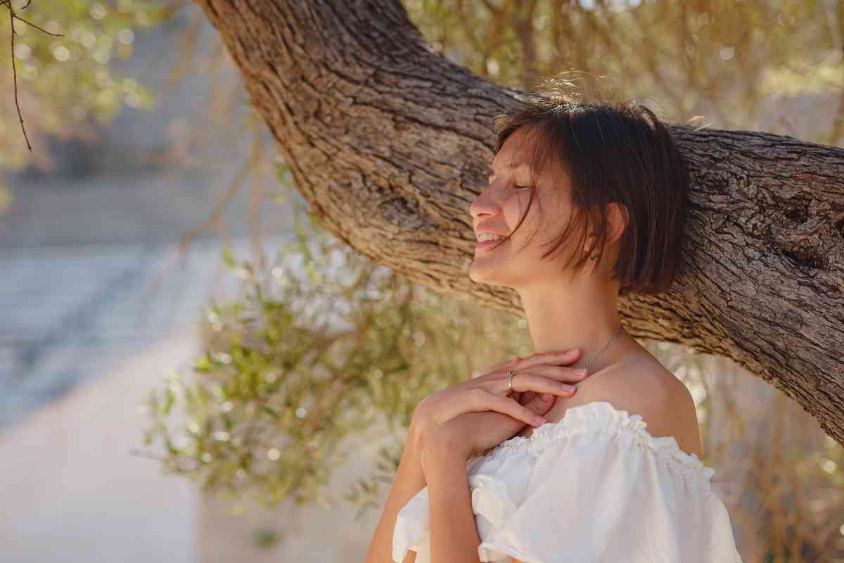 ragazza a occhi chiusi poggiata a un albero