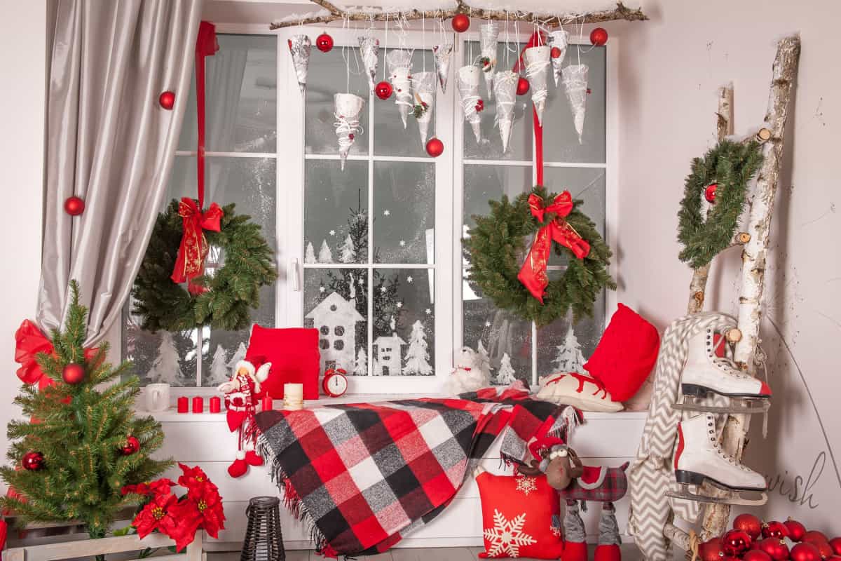 stanza e finestra con decorazioni natalizie, di colori verde e rosso, ghirlande natalizie, mini alberi di natale, coperta scozzese
