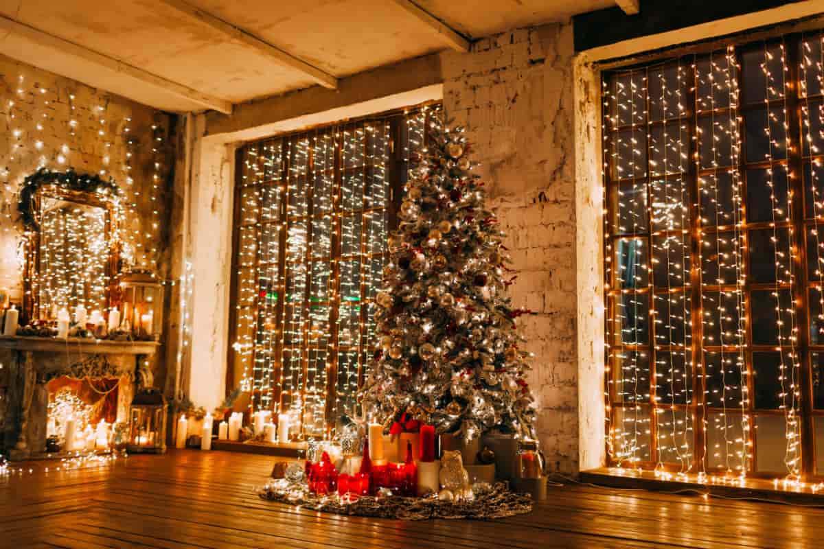 soggiorno con camino, albero di natale pieno di lucine calde e due finestre con tenda di luci