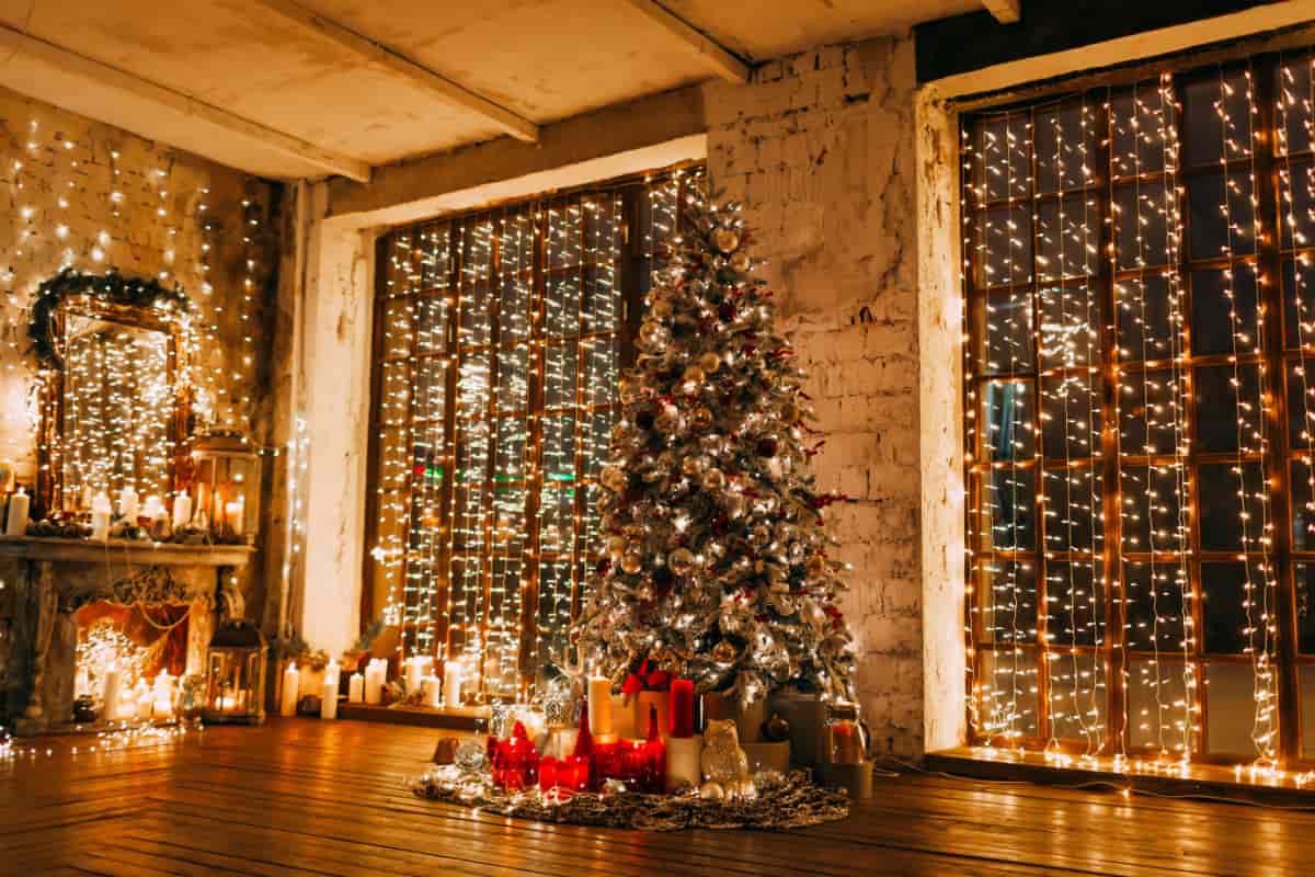 soggiorno con camino, albero di natale pieno di lucine calde e due finestre con tenda di luci 