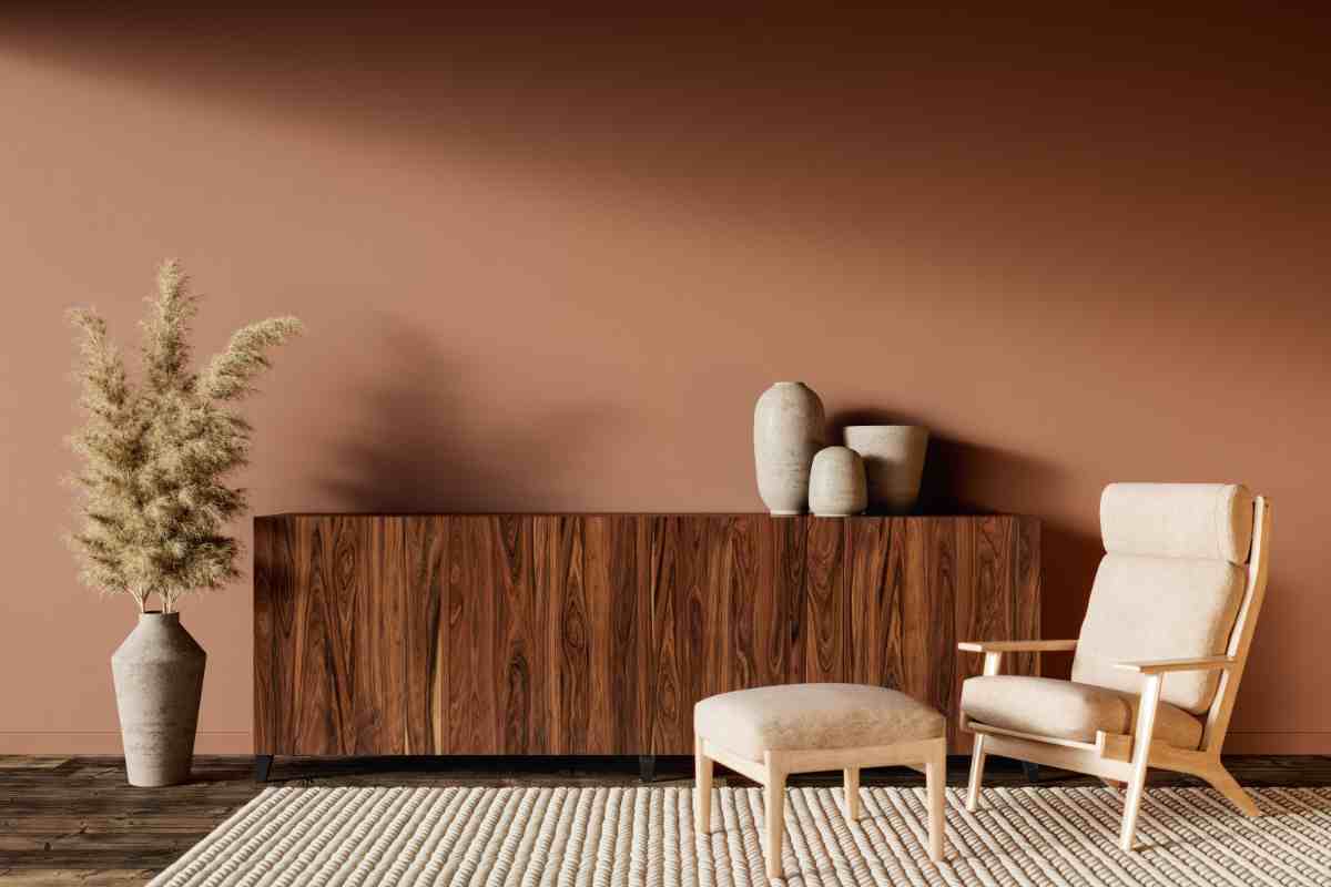 poltrona e pouf bianchi davanti a madia in legno scuro con vasi e parete color terracotta