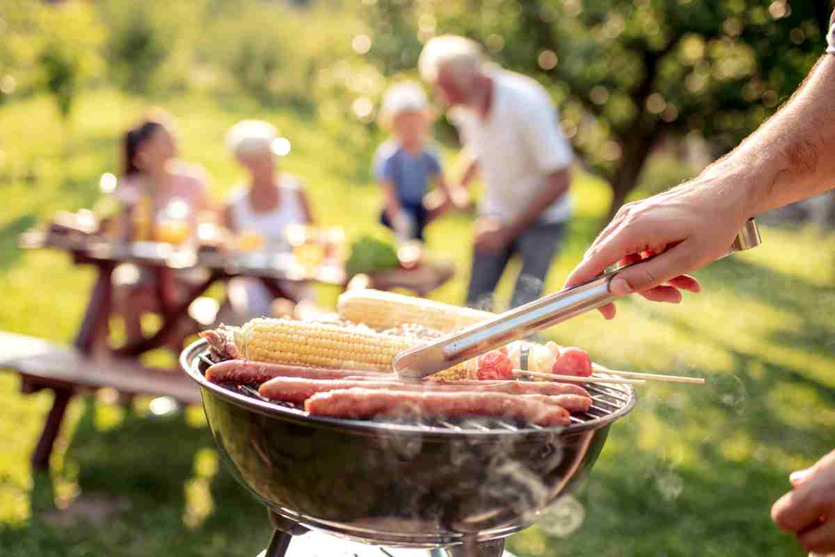 barbecue rotondo su cui stanno cuocendo i cibi e amici sullo sfondo