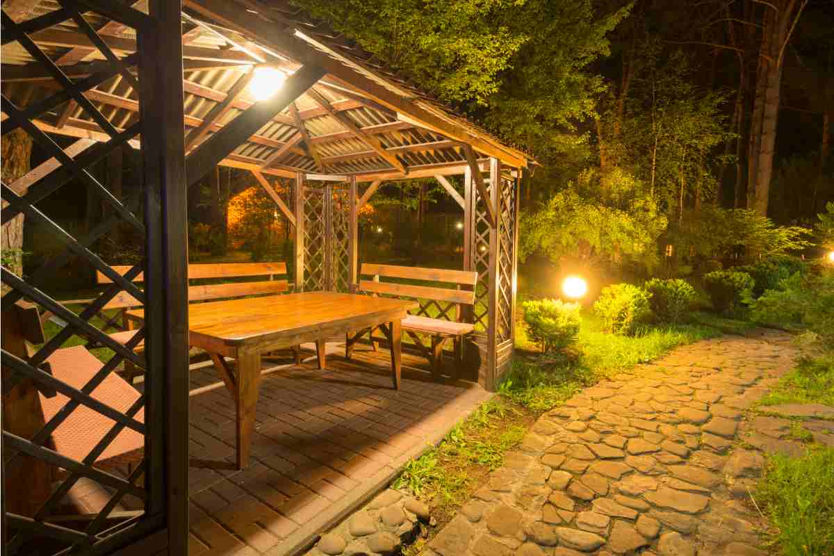 gazebo in legno di tendenza illuminato in giardino arredato con tavolo e panche