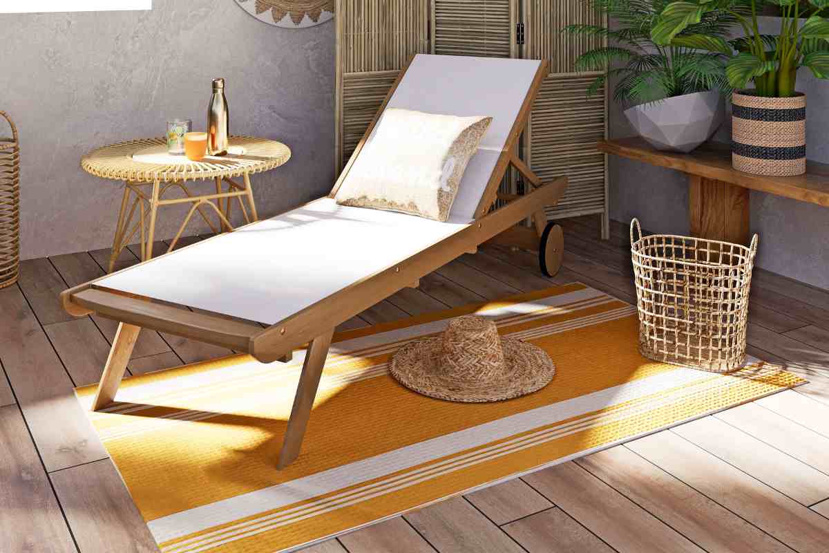 lettino da giardino con cuscino bianco su tappeto giallo vicino a un tavolino in legno da esterno