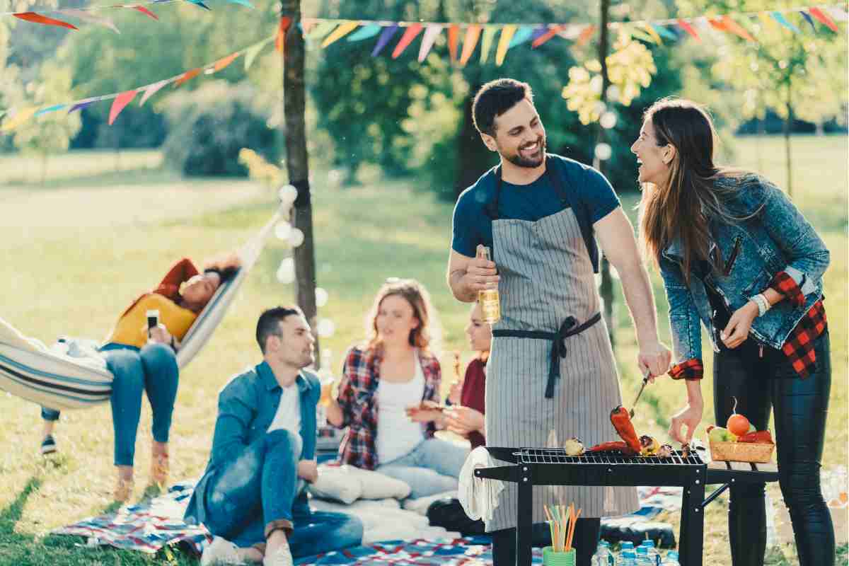 zona relax con amici sul prato e barbecue in primo piano