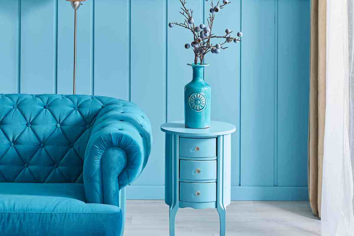 Soggiorno blu stile mermaidcore con divano trapuntato e tavolino con 3 cassetti su cui è posto un vaso azzurro