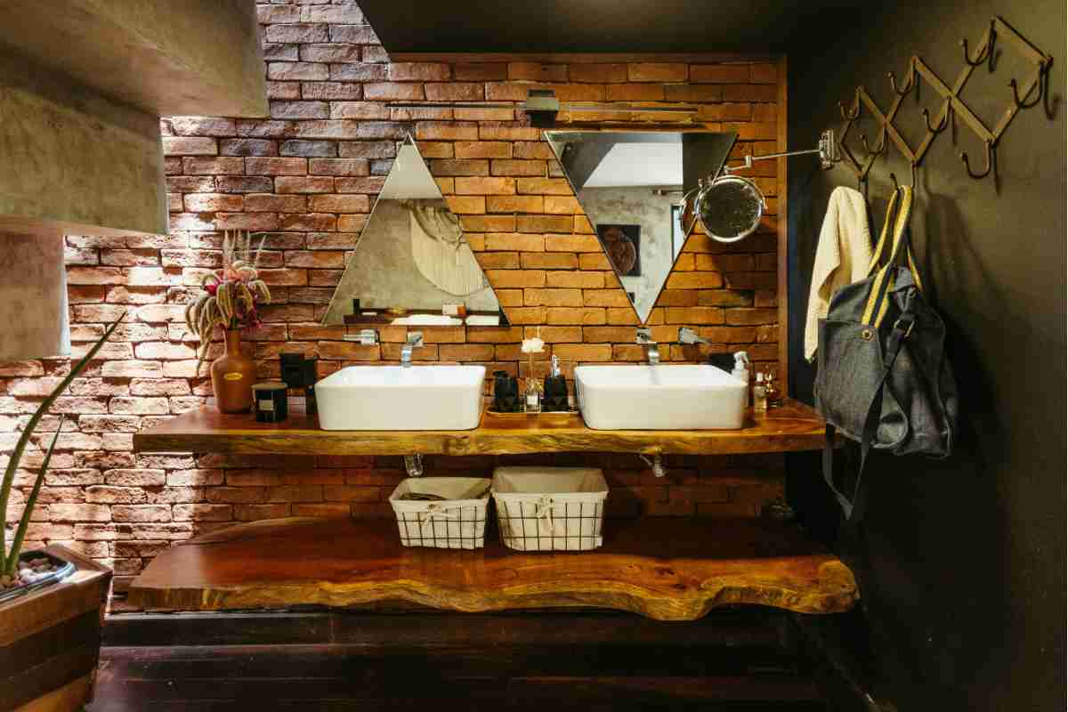 Bagno stile rustico con mattoni a vista e due lavabi poggiati su mensola in legno