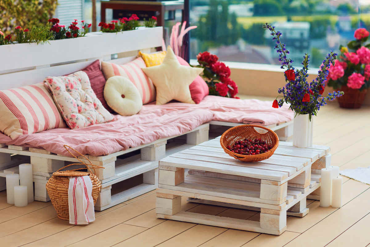 terrazza con pancali in legno e cuscini di colore rosa, con tavolinetto e cesta di ciliegie