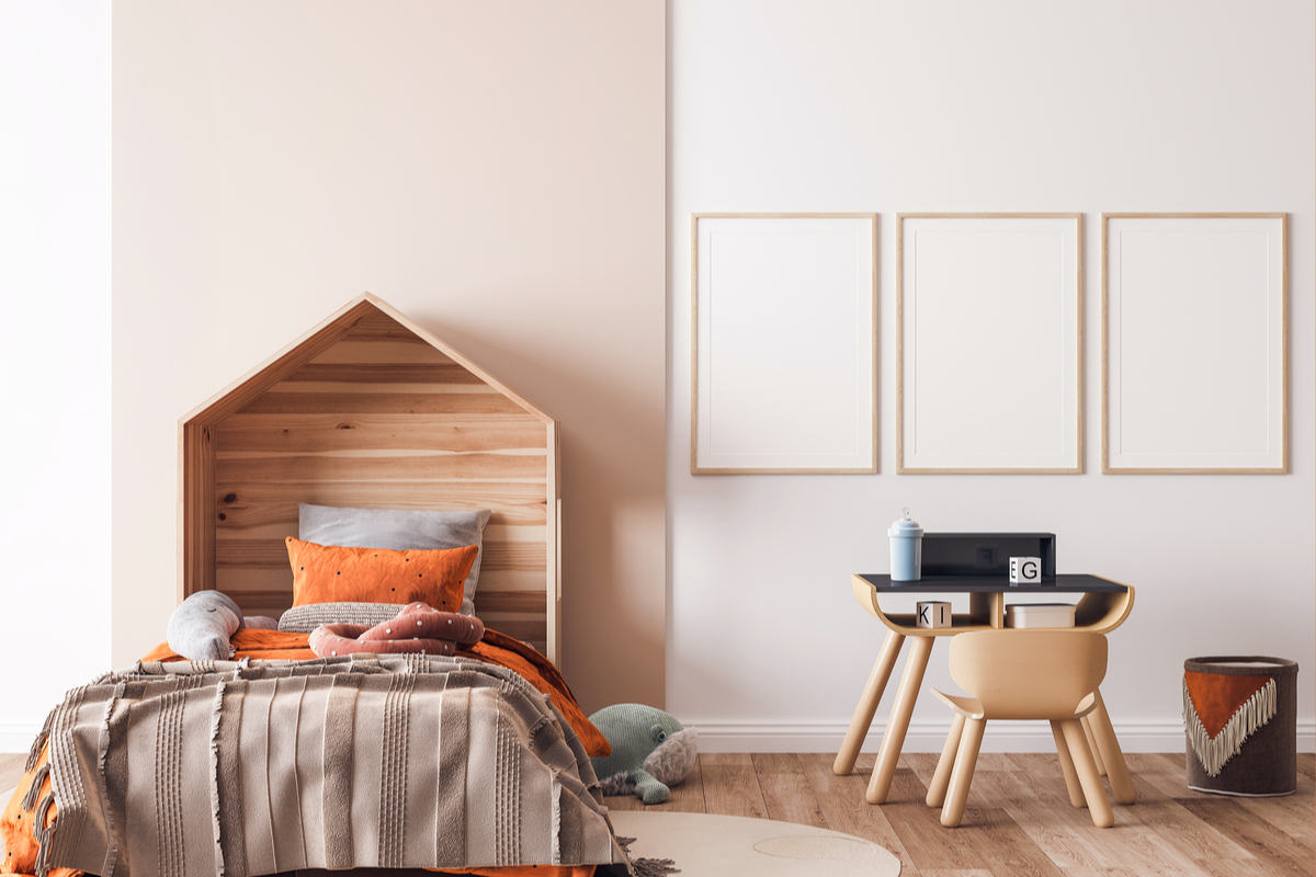 cameretta con pareti di colore bianco e beige, tre quadri appesi bianchi, sedia con tavolinetto in legno, letto in legno con coperte e cuscini marroni e arancioni