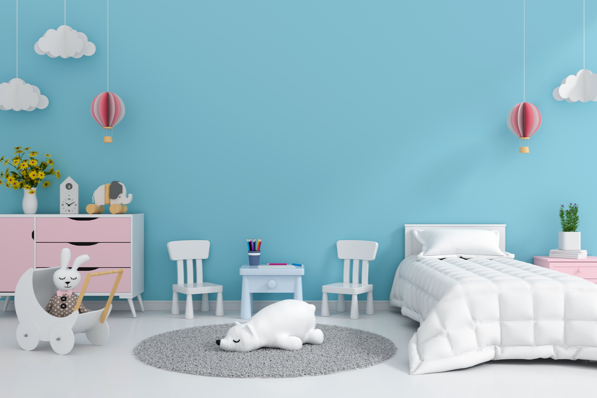 cameretta con pareti di colore azzurro, con nuvolette di carta bianche, letto bianco, mobile rosa, sedie bianche, tappeto grigio e peluche bianco