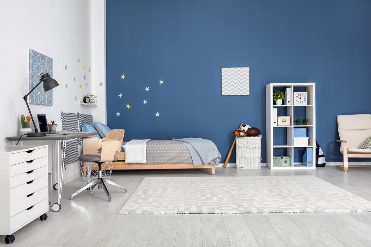 cameretta con parete blu e una bianca, letto, piccola libreria, tappeto grigio, pavimento chiaro, scrivania e mobile bianco