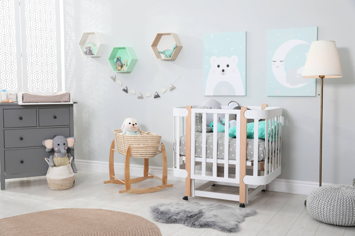 cameretta dai colori grigio e beige con lettino per neonati, quadri appesi di colore bianco e celeste, lampada bianca, mobile grigio, due peluches e tappeto beige