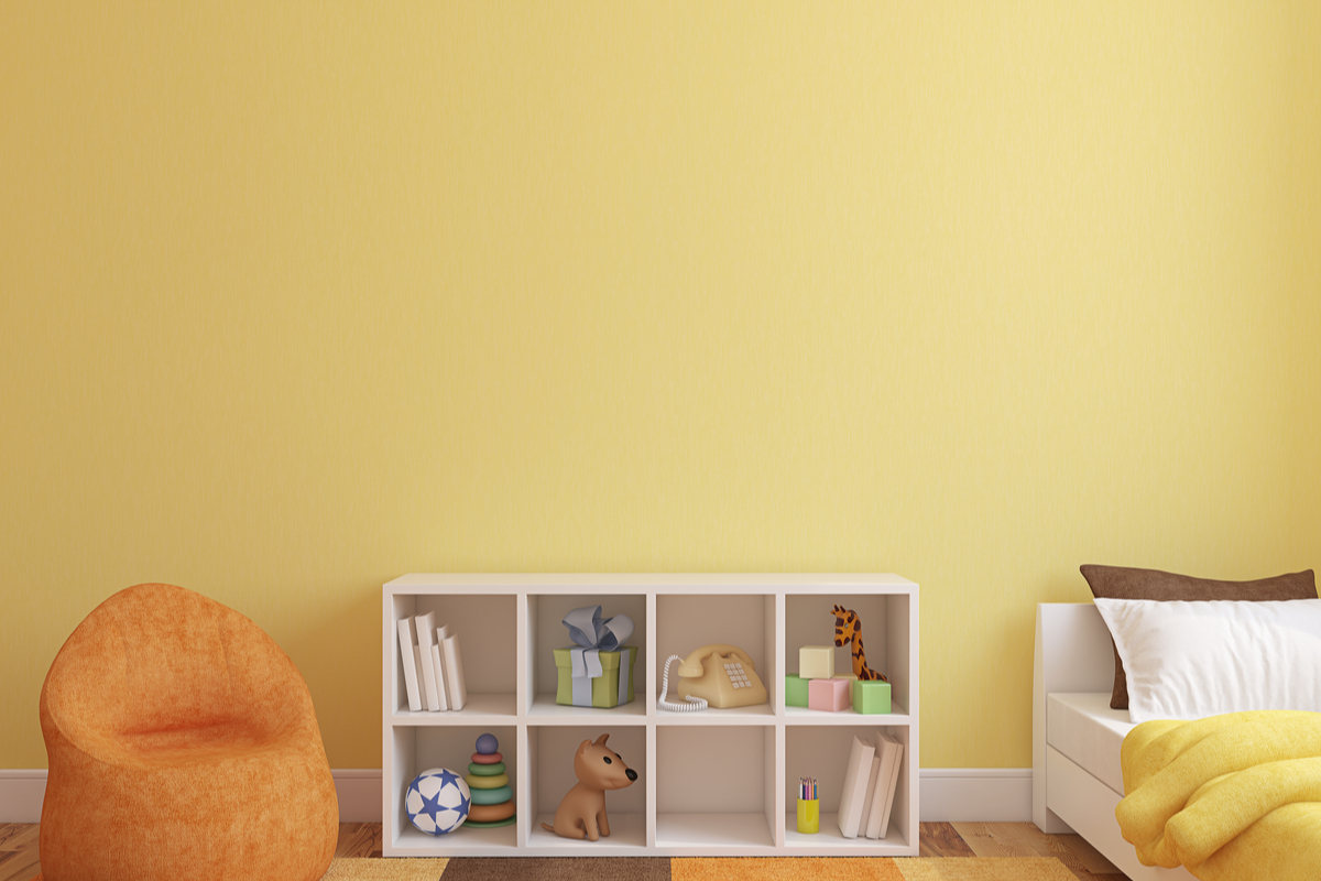cameretta con pareti di colore giallo, poltrona arancio, tappeto arancione, giallo e marrone, con piccola libreria e letto bianco con coperta di colore giallo