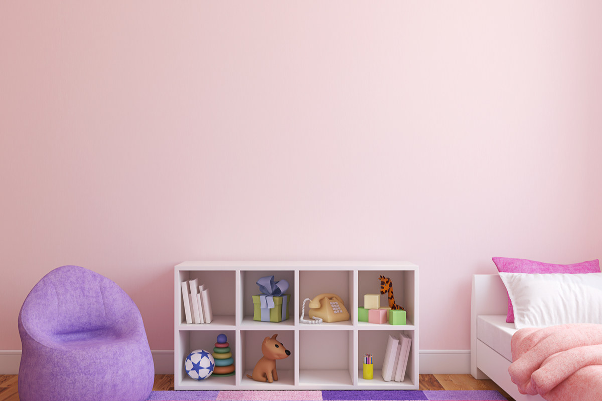 cameretta con parete rosa, poltrona lilla, letto con coperte rosa, piccola libreria e tappeto di colore rosa, viola e fucsia