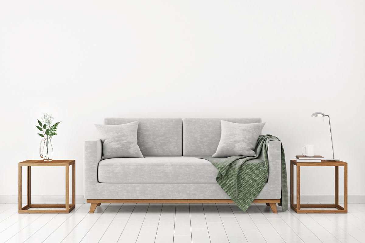divano di colore grigio su parete e pavimento bianchi con due tavolinetti in legno al lato