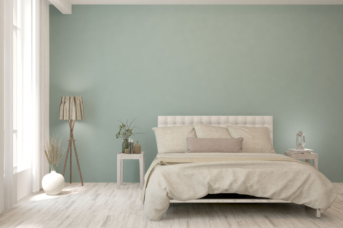 camera con parquet in legno chiaro, letto con coperte e cuscini di colore beige, due comodini ai lati del letto, una lampada e pareti di colore verde chiaro