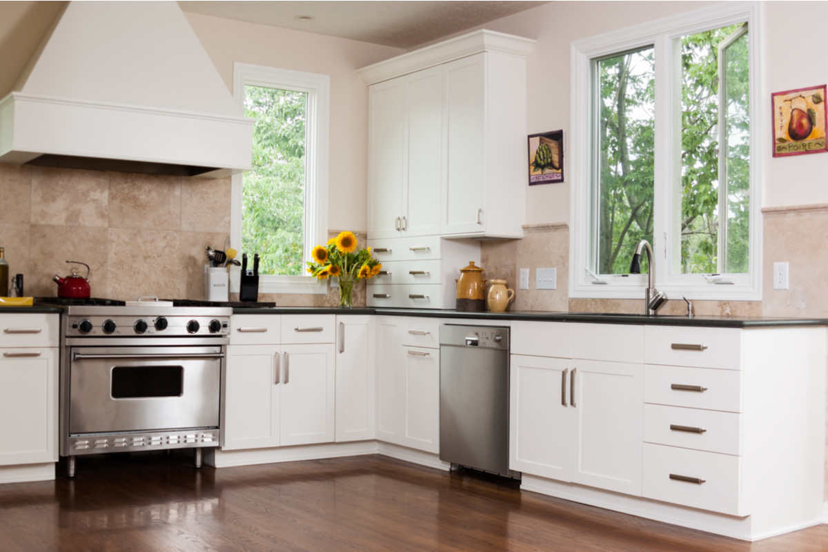 cucina di colore bianco con pareti beige, due finestre e vaso di girasoli