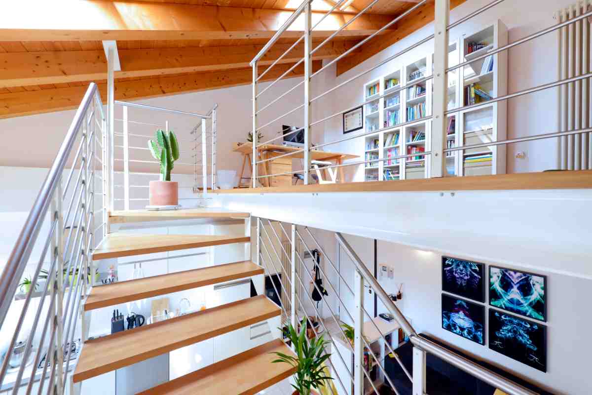 soppalco con scale in legno arredato con mobili di colore bianco e legno naturale