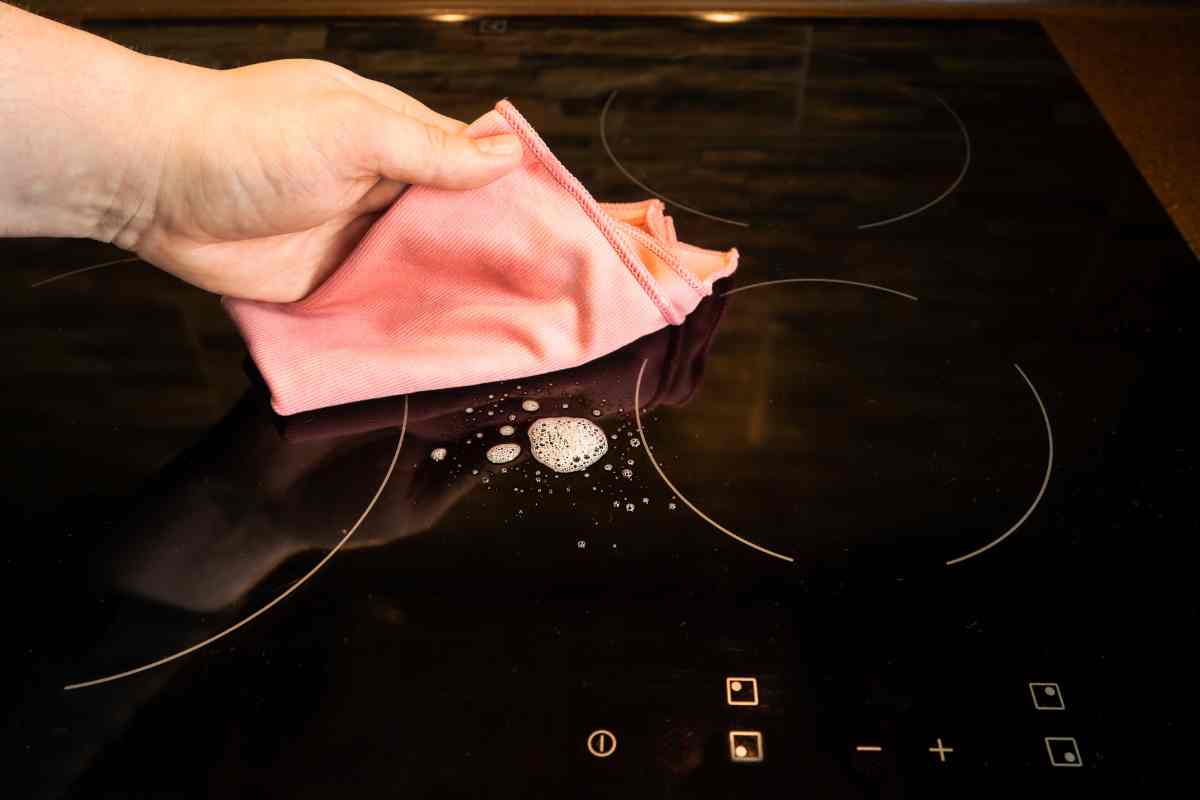 mano con panno in microfibra per pulire piano a induzione