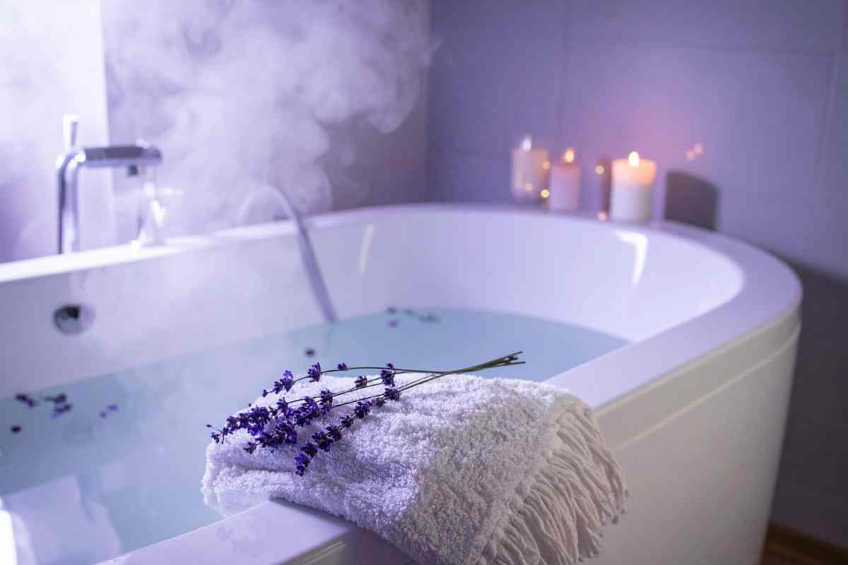 vasca da bagno piena d'acqua con fiori di lavanda e candele accese