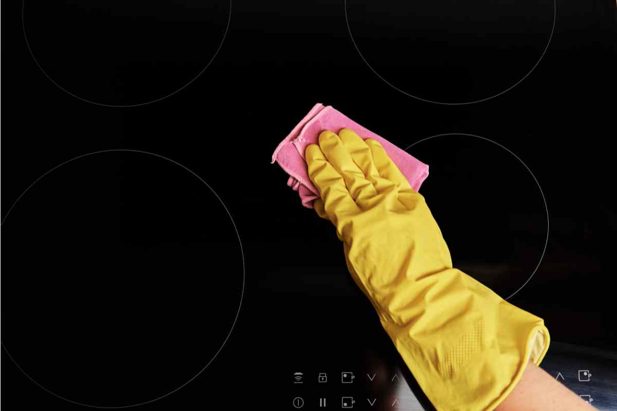 mano con guanto toglie aloni dalla piastra a induzione