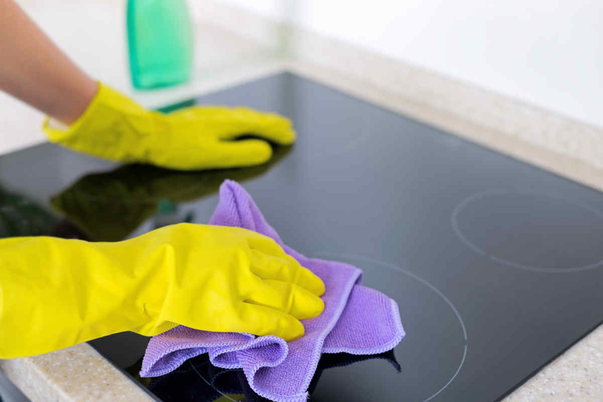 donna con guanti pulisce il piano a induzione della cucina