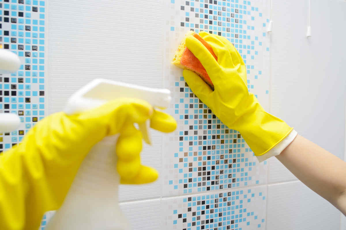 donna pulisce le piastrelle del bagno con spugna e detergente