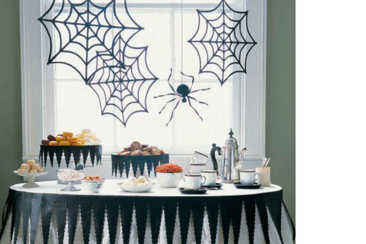 tavola allestita per halloween con dolci e ragnatele finte appesa alla finestra 