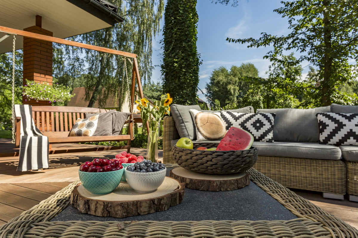 veranda arredata con dondolo da giardino, divanetto e tavolino da esterno