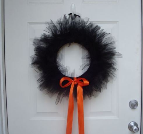 ghirlanda di tulle nero con fiocco centrale di colore arancio, appeso su una porta di colore bianco