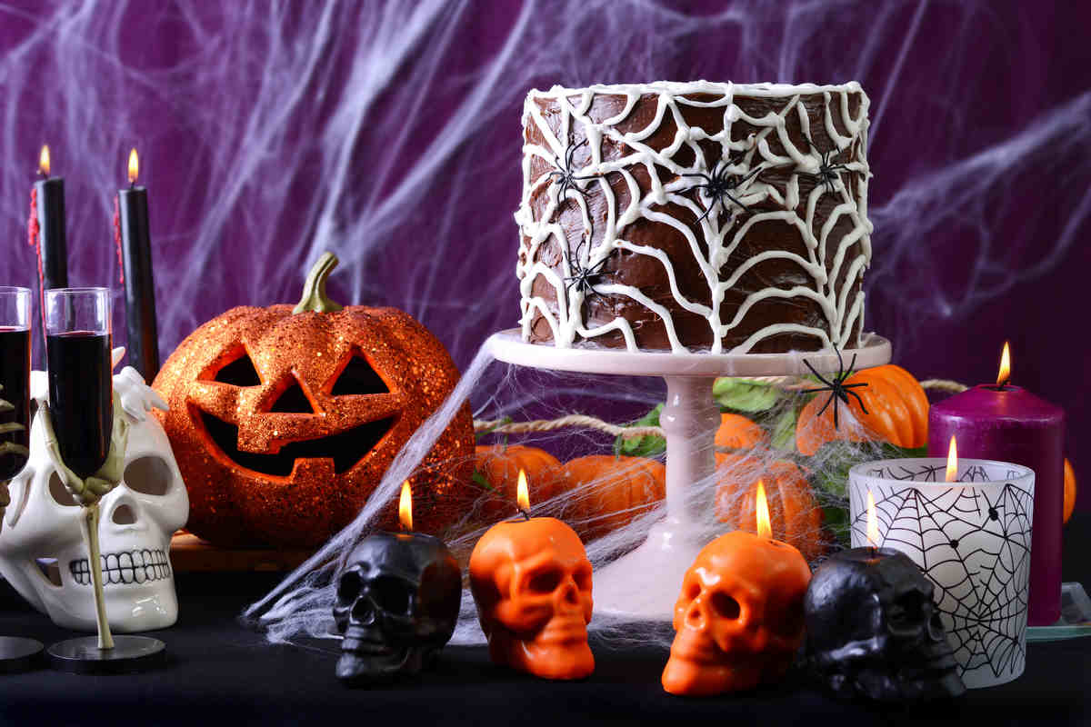 tavolo allestito per halloween con candele a forma di teschio, torta con ragnatela, zucca glitter e sfondo viola con ragnatele 